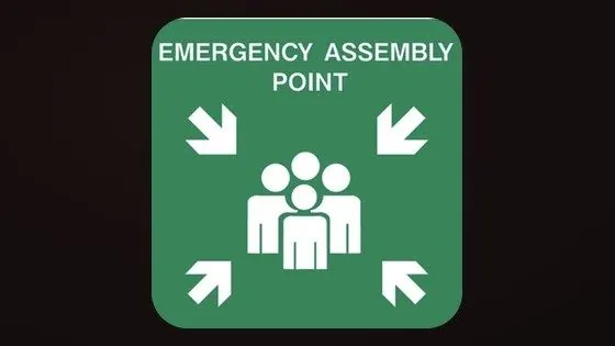 Green Emergency Assembly Point safety sign with directional arrows and figures