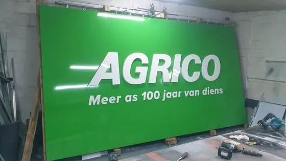 Large green Agrico sign panel with white built-up lettering in a signage workshop