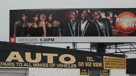 Large roadside billboard mounted above a motor workshop with a painted fascia sign